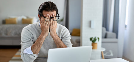 A man got an eye strain from computer and is covering his eyes with his hands