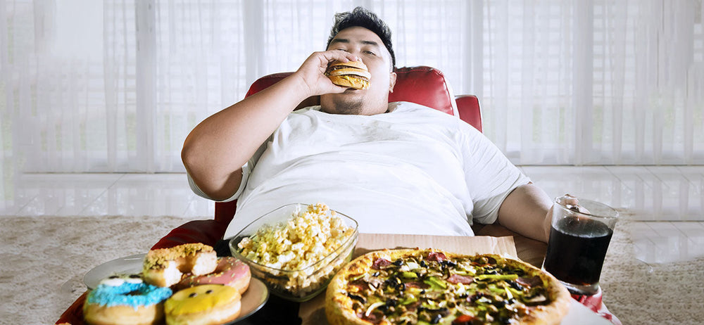 A Heafty man Sitting and eating a burger, and different types of junk food and unhealthy food that are affecting body shape